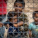 Children look to a US Civil Affairs team through the fence at al Hol camp