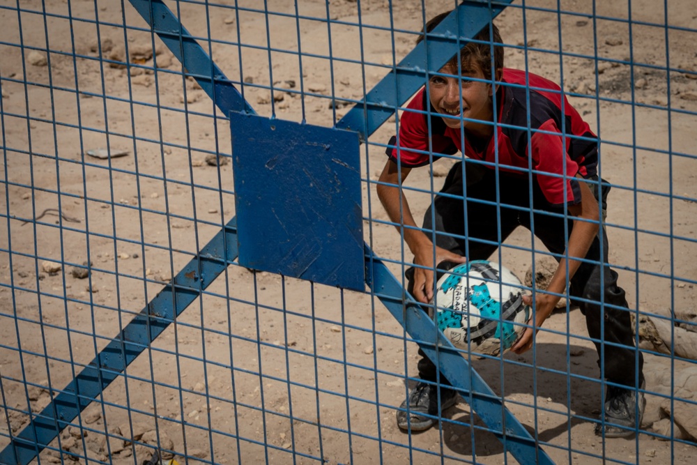 A boy smiles at a US Civil Affairs team through the fence at al Hol camp