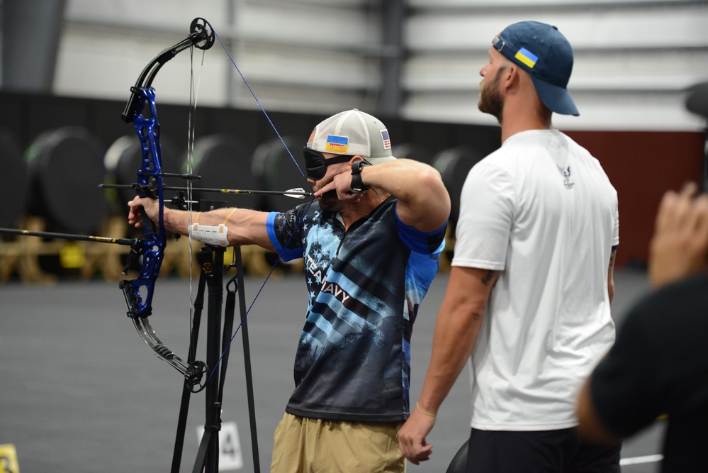 ADAN Clayton Grimstad offers verbal guidance to ME2 (Ret.) Jacob Cox for Visually Impaired Archery