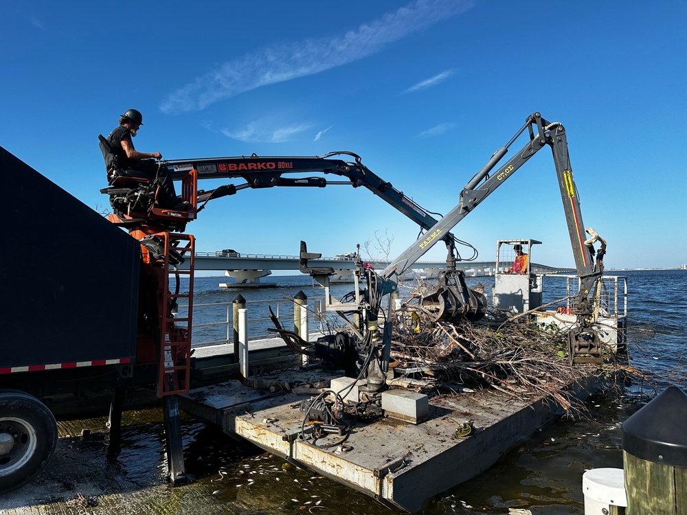 Crews Work To Clear Debris Off Of A Barge That Has Collected Debris in Waterways