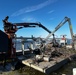 Crews Work To Clear Debris Off Of A Barge That Has Collected Debris in Waterways