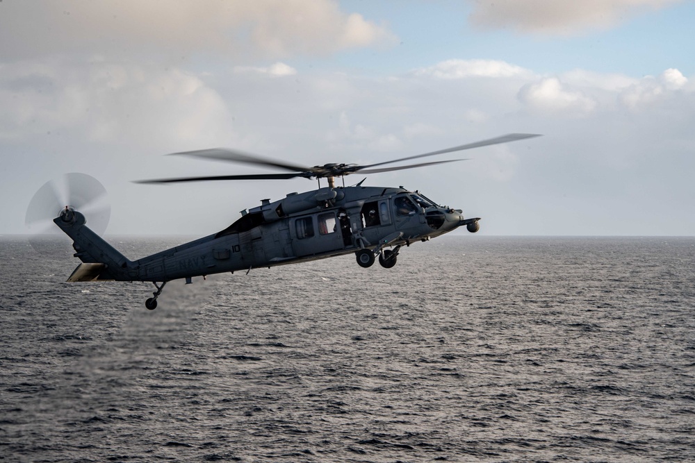 A MH-60S Sea Hawk passes Nimitz-class aircraft carrier USS Carl Vinson