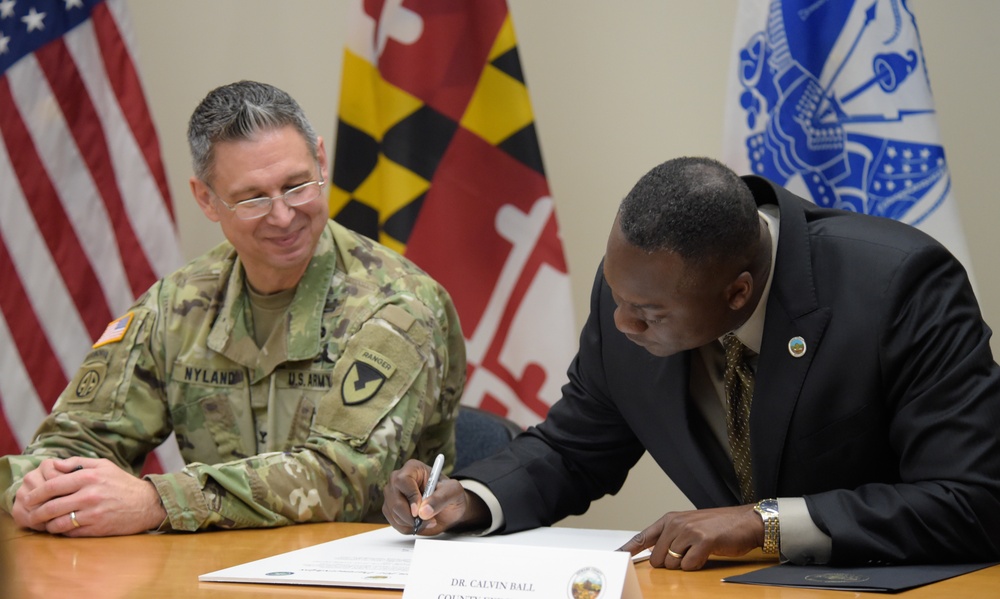 Col. Christopher Nyland, Fort Meade commander, looks on as Dr. Calvin Ball, Howard County Executive, signs a Fort George G. Meade and Howard County Intergovernmental Support Agreement document