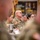 A group of U.S. Army soldiers in OCP (Operational Camouflage Pattern) uniforms are seated at a table during what appears to be a briefing or meeting. The central figure is a bald male soldier wearing glasses and displaying a 1st Cavalry Division patch on his left shoulder. The image is captured through a shallow depth of field, with blurred foreground figures framing the in-focus subjects.