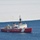 A U.S. Coast Guard vessel with hull number 10 is navigating open blue water adjacent to a large ice shelf or ice sheet. The ship features the distinctive red hull and white superstructure typical of USCG icebreaker vessels. The setting appears to be a polar or sub-polar region based on the presence of sea ice in the background.