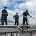Sailors slack lines during line handling operations in preparation for mooring from the flight deck