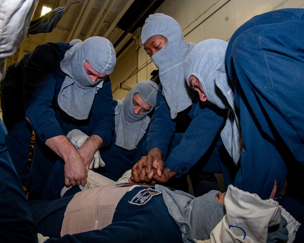 Sailors perform stretcher bearer tactics on a simulated patient during a general quarters drill.
