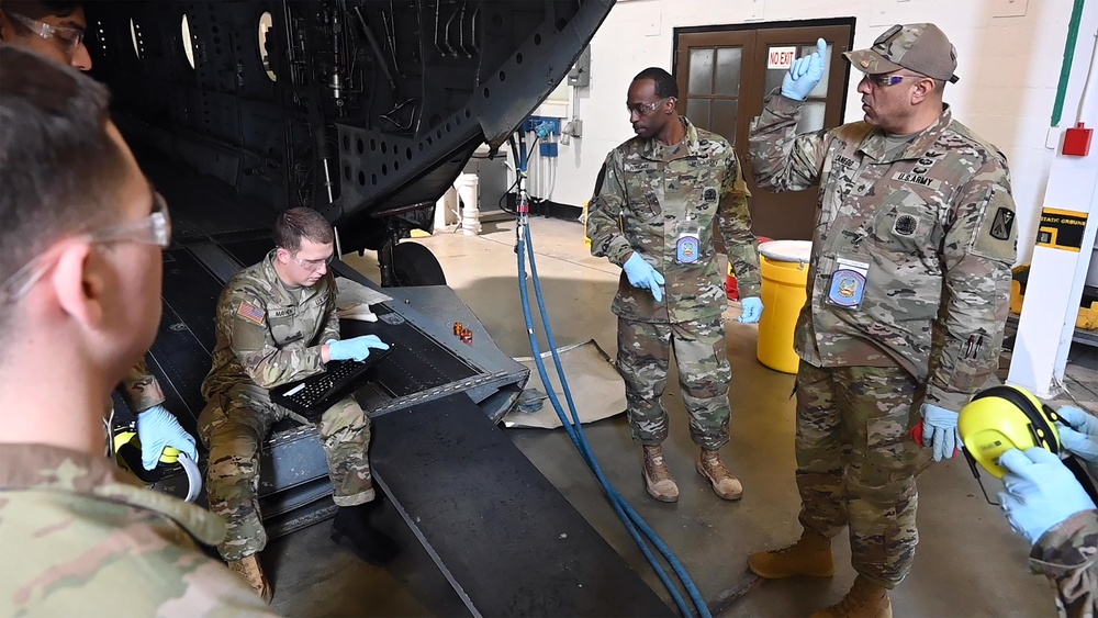 Soldiers training on hydraulic procedures from the rear ramp of a Boeing CH-47 Chinook helicopter simulator, with guidance from instructors.