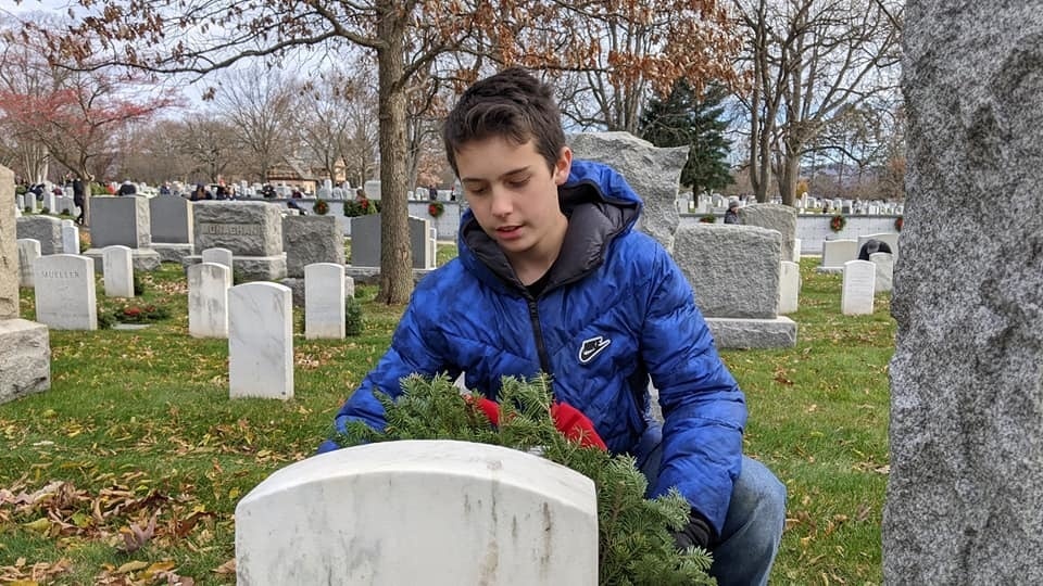 A child places a wreath against a grave stone during a Wreaths Across America event at the West Point cemetery