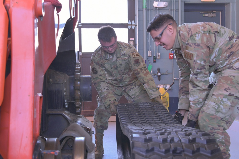 Vehicle Maintenance crew lifting a track for a compact track loader