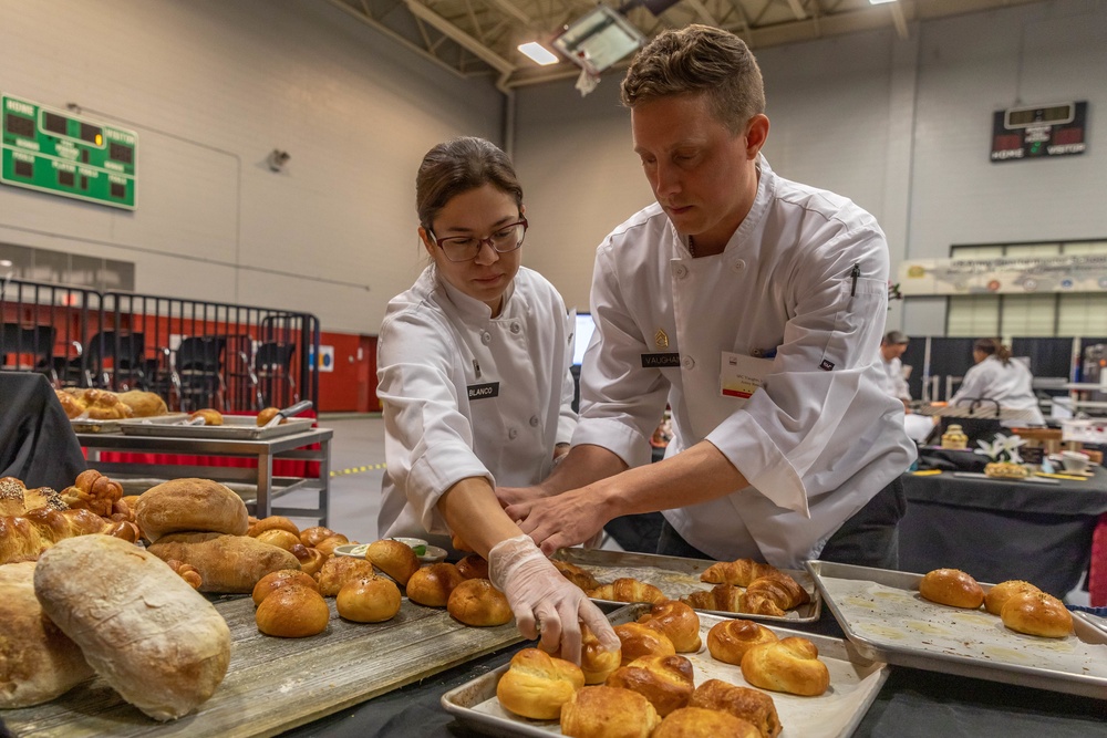 Sgt. 1st Class Jeffery Vaughan helps Warrant Officer 1 Daniella Blanco set up a bread display