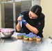 A Sailor finishes decorating a cupcake with mixed color icing.