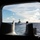 USS Carl Vinson (CVN 70) Fueling-at-sea The image is taken from inside a naval vessel looking through a rectangular porthole or hatch opening toward another warship in the distance on open ocean. The distant vessel appears to be a guided-missile destroyer based on its silhouette, sailing ahead in calm-to-moderate seas. The foreground shows metal deck hardware, likely bollards or cleats, framing the view.