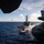 USS Carl Vinson (CVN 70) Fueling-at-sea The image shows a U.S. Navy Arleigh Burke-class guided-missile destroyer sailing alongside what appears to be a large aircraft carrier, photographed from the carrier's deck. The ships are operating in open blue ocean under partly cloudy skies. A naval aircraft, likely an F/A-18 Hornet or Super Hornet, is visible on the carrier's flight deck in the foreground.