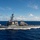USS Carl Vinson (CVN 70) Fueling-at-sea A U.S. Navy Arleigh Burke-class guided-missile destroyer is underway at sea, cutting through deep blue ocean waters at moderate to high speed. The vessel displays hull number '63' on its bow, consistent with USS Stethem or a similarly numbered destroyer. The image was taken from a low angle, likely from another vessel or aircraft, under partly cloudy skies.