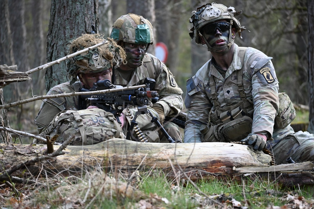 One soldier holds a weapon while two other soldiers look on.