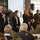 DPAA hosts Chicago FMU A formal conference or symposium is taking place in a banquet-style room, where a panel of speakers is being introduced or recognized at the front of the room. The group includes civilians in business attire and two individuals in U.S. Marine Corps dress uniforms. A POW/MIA flag is prominently displayed on the left side of the stage area.