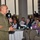 DPAA hosts Chicago FMU A U.S. Marine Corps Staff Non-Commissioned Officer in dress green uniform is addressing a large audience at what appears to be a formal luncheon or civic event. He is holding a microphone and speaking to a room full of seated civilians at round tables. The setting suggests a community outreach, awards ceremony, or public affairs engagement.