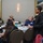 DPAA hosts Chicago FMU A formal gathering or conference is taking place in a banquet-style room, with people seated at a round table labeled 'Table 29'. A woman dressed in black is standing and speaking or presenting to the seated group. The setting appears to be a hotel or convention center meeting room.