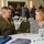 DPAA hosts Chicago FMU A U.S. Marine Corps officer in dress uniform is engaged in conversation with a civilian woman at a round table during what appears to be a formal conference or symposium. The setting is a hotel or conference center ballroom with multiple tables and attendees visible in the background. Table signage and materials related to 'Air Force Casualty' and military organizations are visible on the table.
