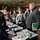 DPAA hosts Chicago FMU A military service member in Army dress uniform is staffing a registration or check-in table at what appears to be an official event or conference held in a hotel or convention center. Civilians are lined up at the table, with name tags and printed materials spread across the black-draped table. The scene suggests a formal military-civilian community engagement or informational event.