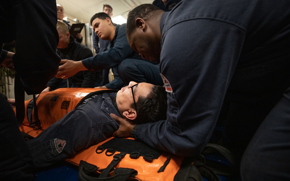 Electronic Technician 2nd Class Andre Woods assists sailors in stretcher bearer training