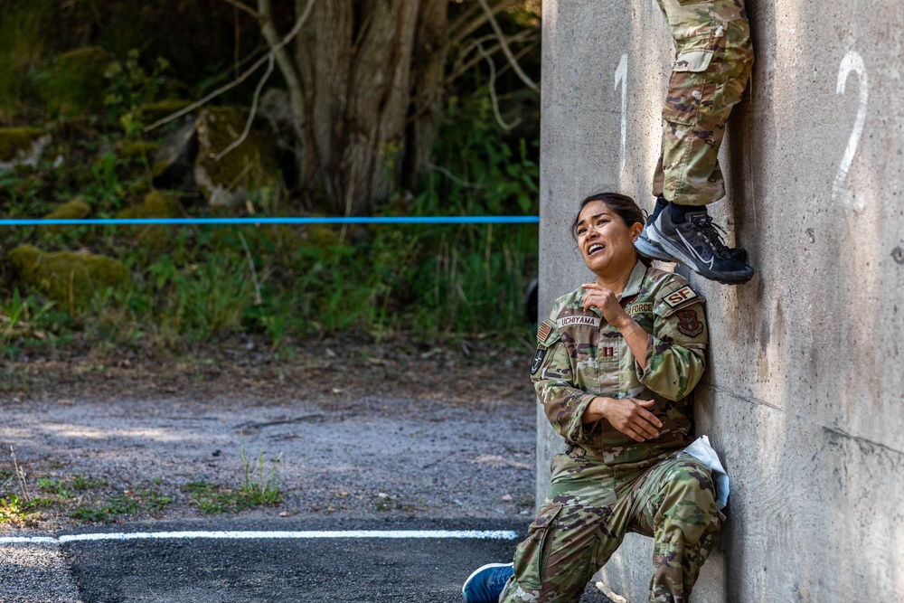 Air Force Reserve Capt. Andrea Uchiyama assists her teammate over an obstacle