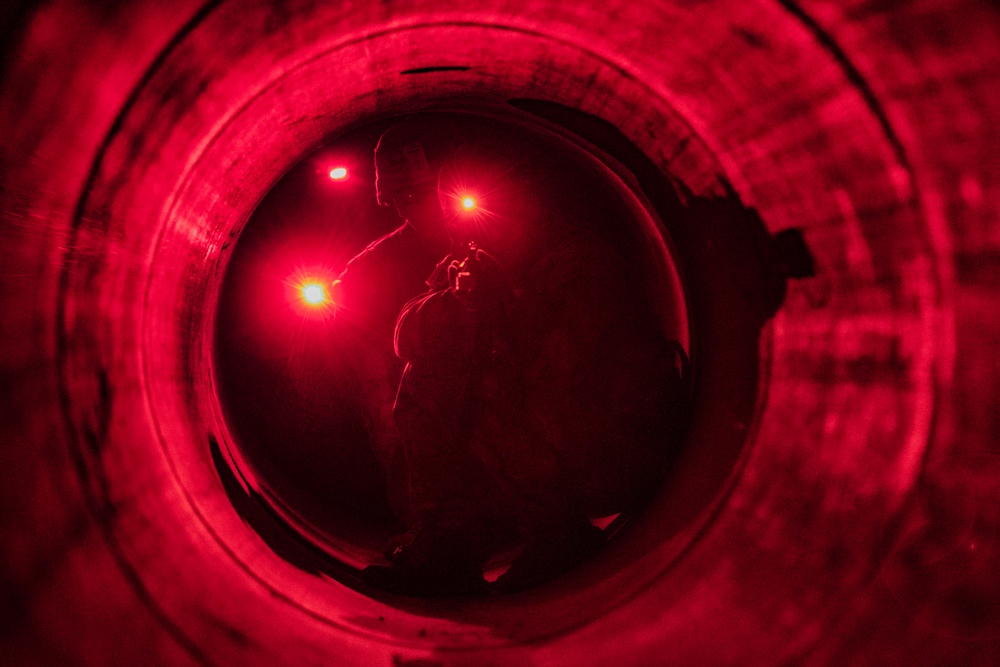 A U.S. Army Reserve Best Squad competitor aims down his sights while crouched in a tunnel