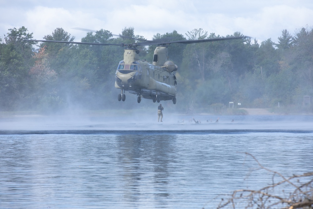 U.S. Army Reserve Best Squad competitors float in the water as their teammate jumps out of a CH-47 Chinook