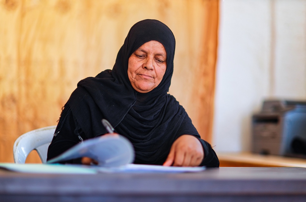 Al Jafr Women Association Director and Ana Usharek Mujtama3i trainee, Hamda Abu Tayeh, sits writing at her desk.