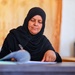 Al Jafr Women Association Director and Ana Usharek Mujtama3i trainee, Hamda Abu Tayeh, sits writing at her desk.