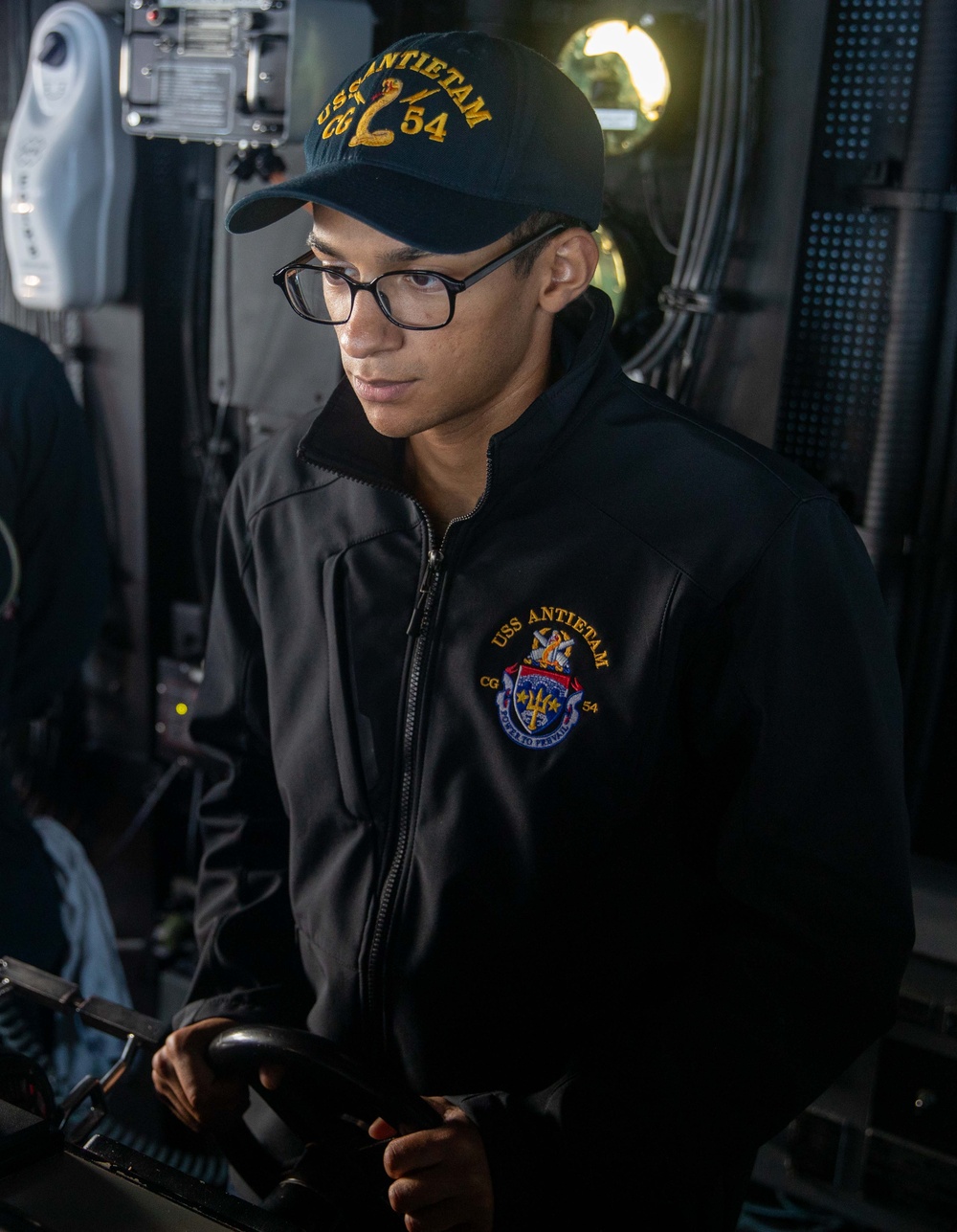 QM3 Michel operates the ship's helm in the bridge of USS Antietam (CG 54) during Multi-Large Deck Event (MLDE)