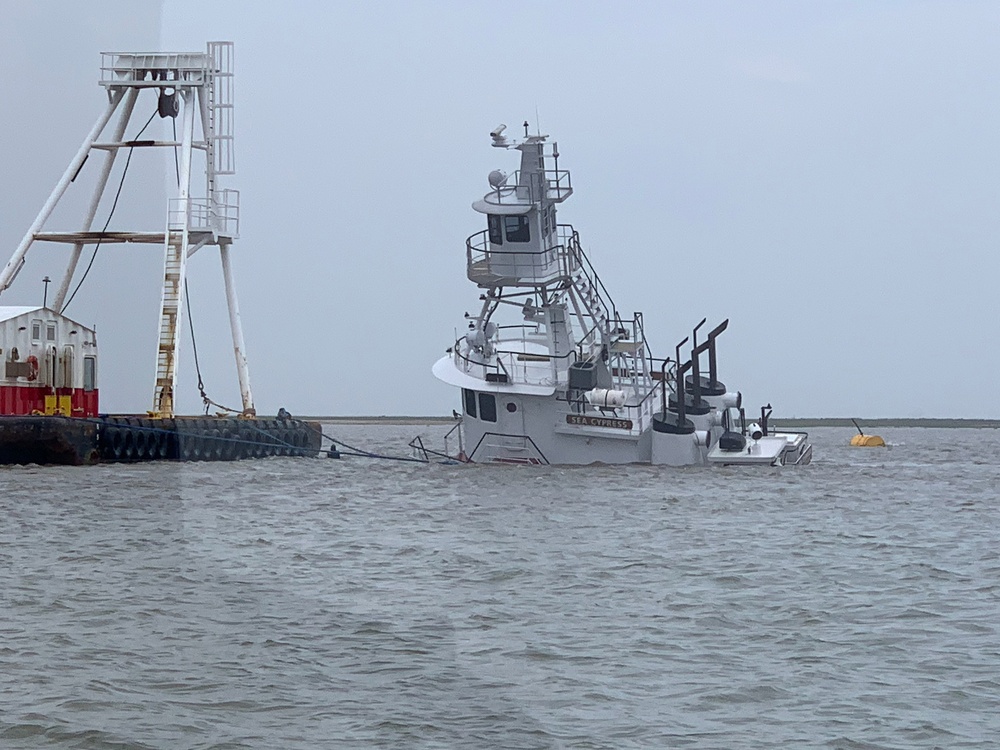 The Sea Cypress, a 75-foot tugboat, capsizes while tied off to a barge at the mouth of the Sabine Pass Channel, March 31, 2023. Coast Guard Petty Officer 2nd Class Chad Rollins, a machinery technician at Station Sabine, pried open a hole in the sinking boat and rescued two men who were trapped inside. (U.S. Coast Guard photo by Seaman Katelynn Reyes)