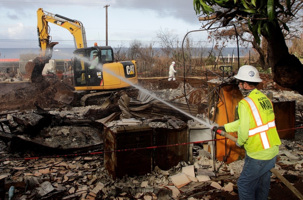 U.S. Army Corps of Engineers contractor located in the cold zone sprays water to minimize dust becoming airborne during debris removal