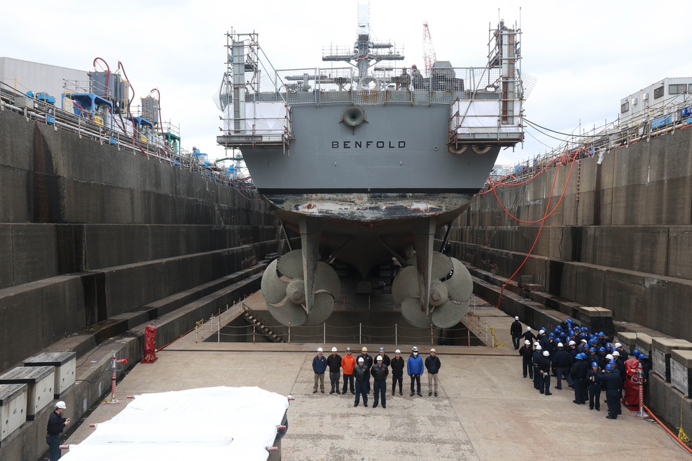 Contractors and Sailors pose for a group photo in front of the USS Benfold (DDG 65) in a dry dock onboard Commander, Fleet Activities Yokosuka