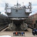 Contractors and Sailors pose for a group photo in front of USS Benfold (DDG 65) in a dry dock onboard Commander, Fleet Activities Yokosuka