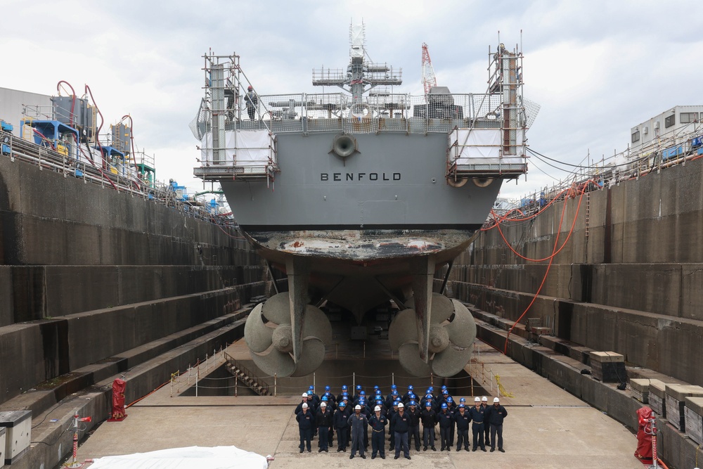 Sailors pose for a group photo in front of the USS Benfold (DDG 65) in a dry dock onboard Commander, Fleet Activities Yokosuka