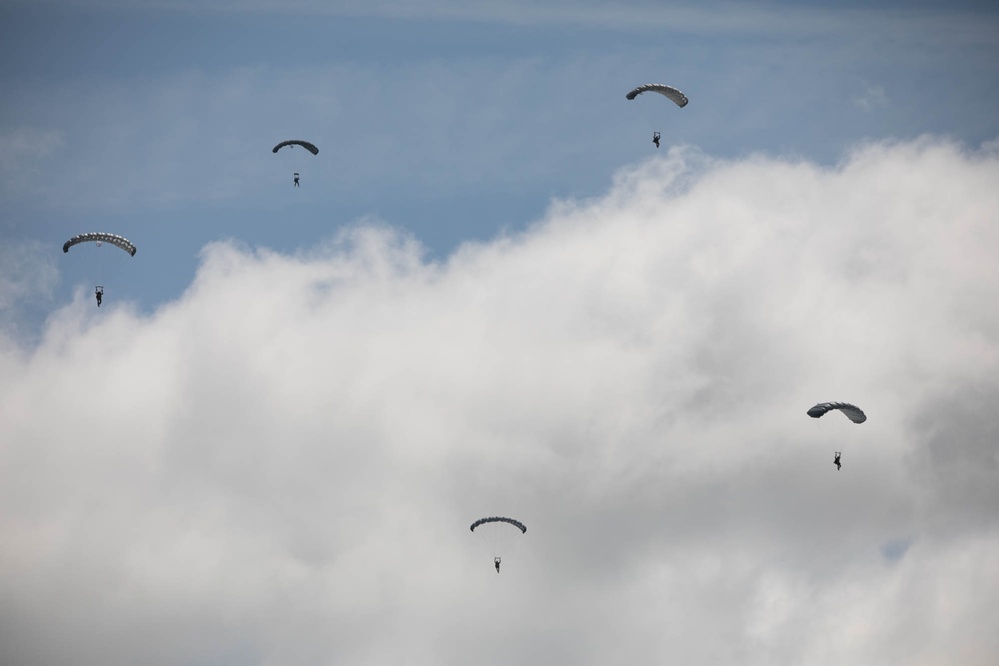 Service members and civilians perform a freefall jump near Amfreville, France