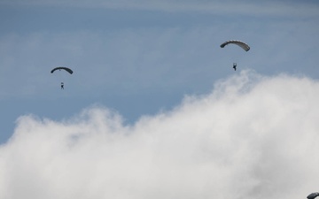 Service members and civilians perform a freefall jump near Amfreville, France