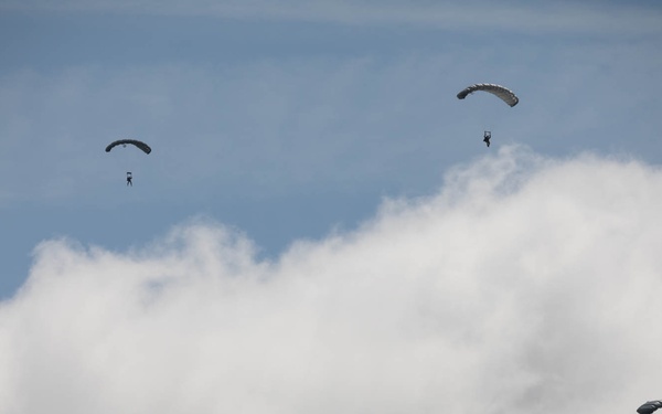 Service members and civilians perform a freefall jump near Amfreville, France