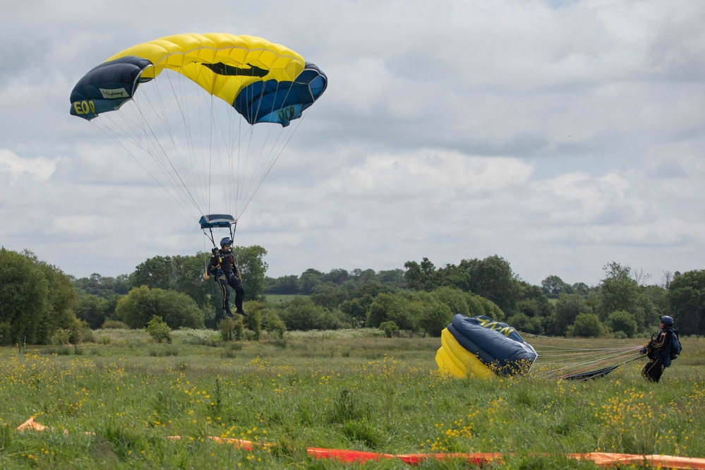 Service members and civilians perform a freefall jump near Amfreville, France