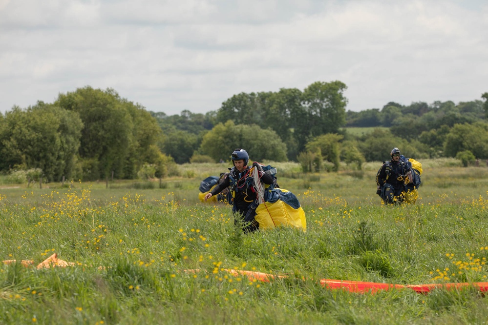 Service members and civilians perform a freefall jump near Amfreville, France