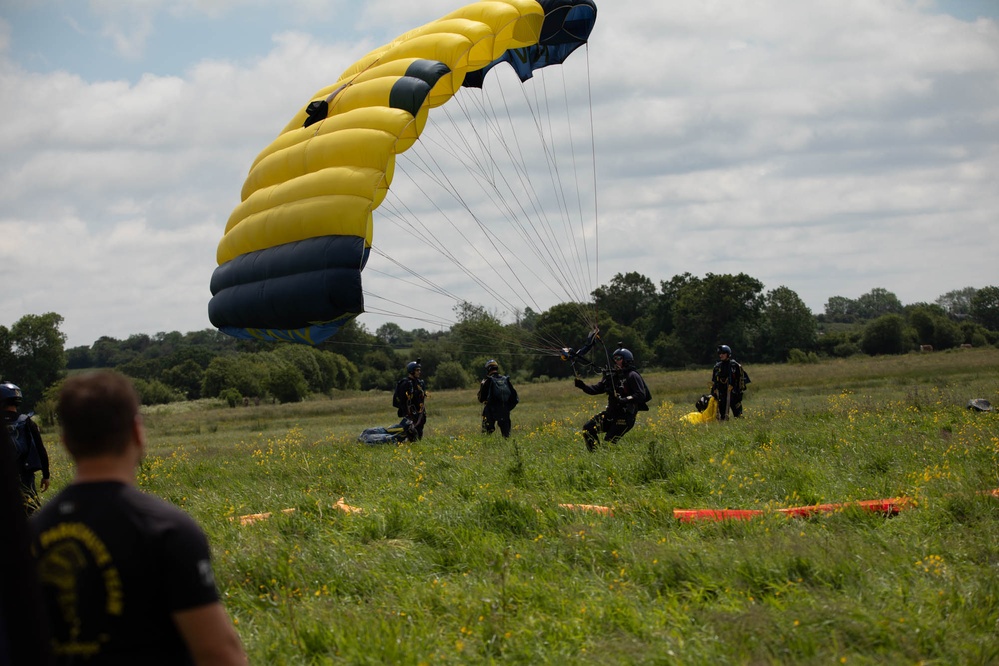 Service members and civilians perform a free-fall jump near Amfreville, France