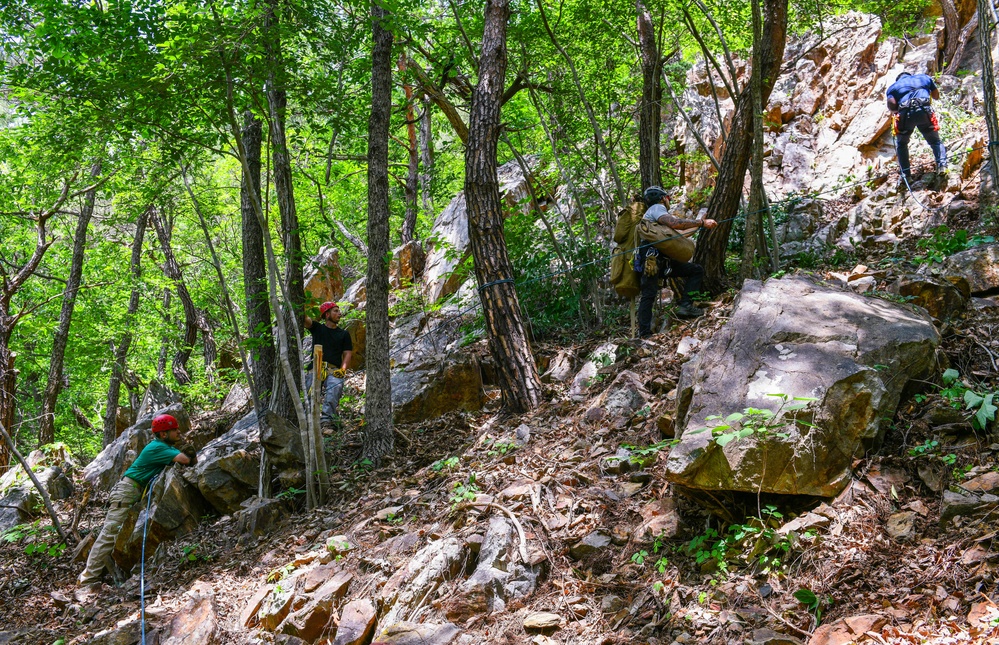 A Defense POW/MIA Accounting Agency recovery team climbing a wooded mountain in South Korea