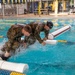 Sgt. Thomas Hunt and Sgt. 1st Class Benjamin Latham jump off of a water obstacle