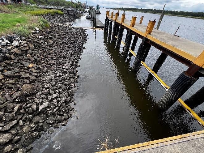 The Brunswick East River Mystery Sheen (BERMS) site during low tide shows light silver sheening from oil discharge and boom configuration in Brunswick, Georgia, July 2, 2024. A Unified Command consisting of the U.S. Coast Guard, the U.S. Environmental Protection Agency and the Georgia Department of Natural Resources, was established to coordinate response actions and disseminate information for the BERMS response. (U.S. Coast Guard photo by Chief Warrant Officer Timothy Tamargo)