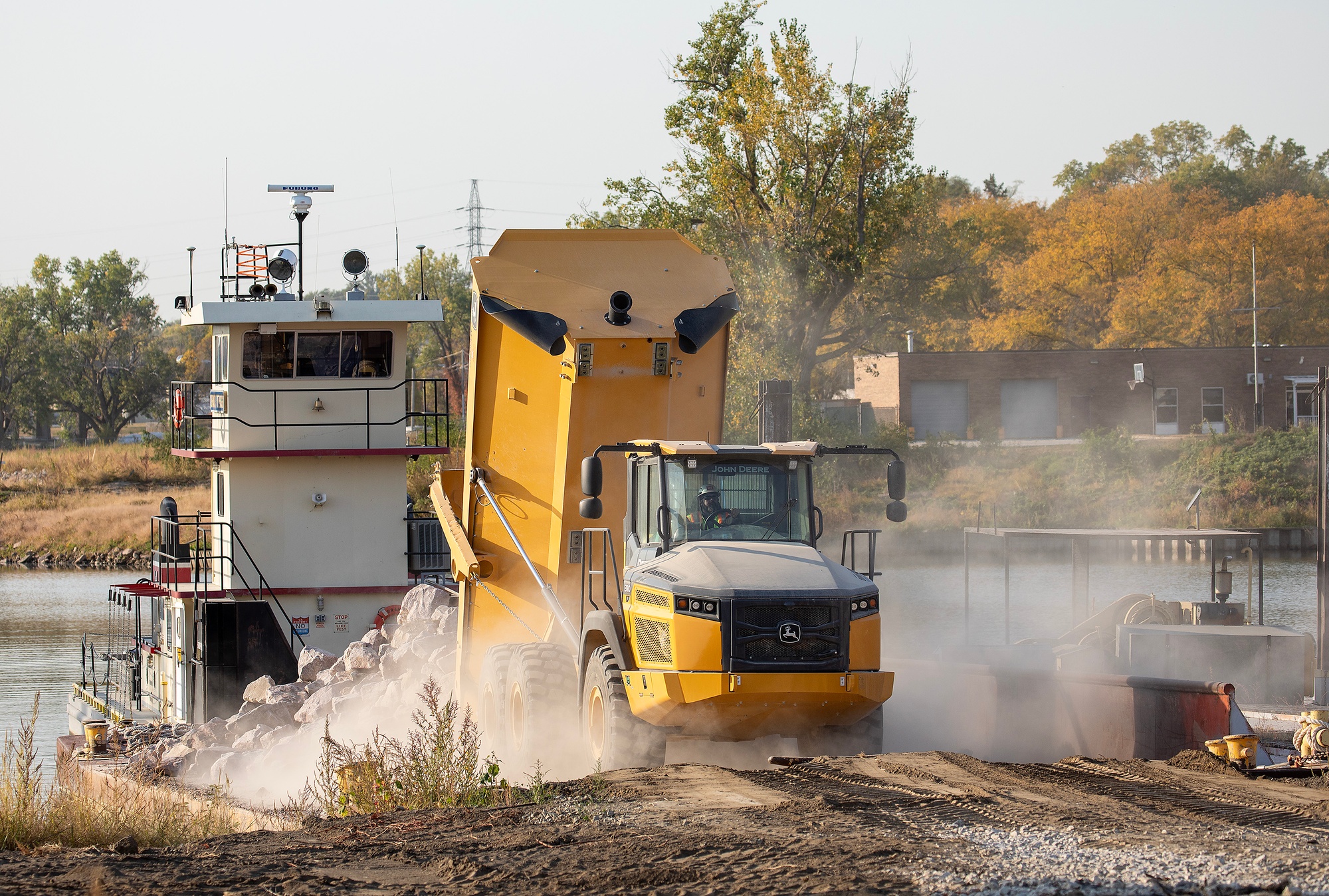 Dump truck unloading riprap onto a barge for streambank erosion protection