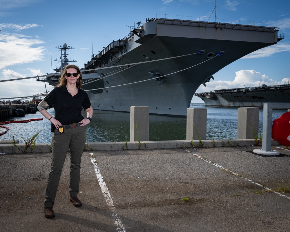 Naval Criminal Investigative Service (NCIS) Special Agent Afloat (SAA) Bernadette Fuffy poses for an environmental portrait in front of the US Navy aircraft carrier USS Harry S. Truman (CVN 75) at Norfolk Naval Station Virginia on 19 September 2024.