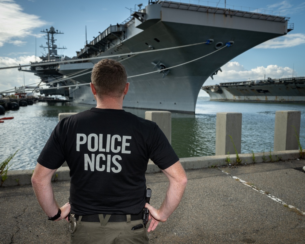 Naval Criminal Investigative Service (NCIS) Special Agent Afloat (SAA) Justin Botkin stand for an environmental portrait in front of the US Navy aircraft carrier USS Harry S. Truman (CVN 75) at Norfolk Naval Station Virginia on 19 September 2024.