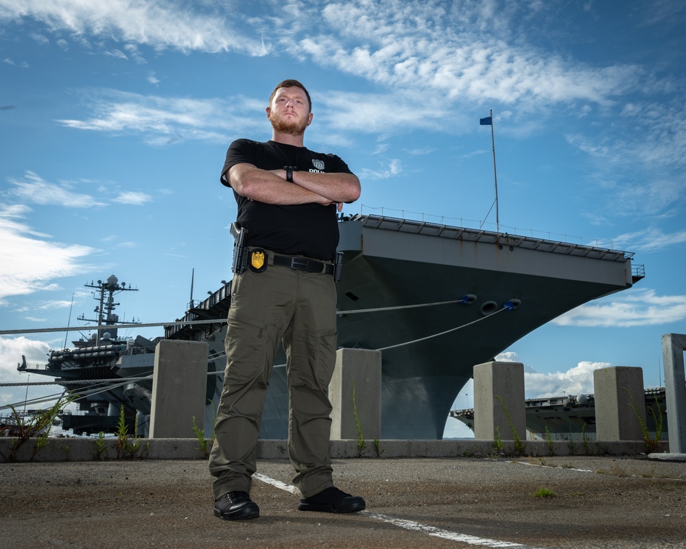 Naval Criminal Investigative Service (NCIS) Special Agent Afloat (SAA) Justin Botkin stand for an environmental portrait in front of the US Navy aircraft carrier USS Harry S. Truman (CVN 75) at Norfolk Naval Station Virginia on 19 September 2024.